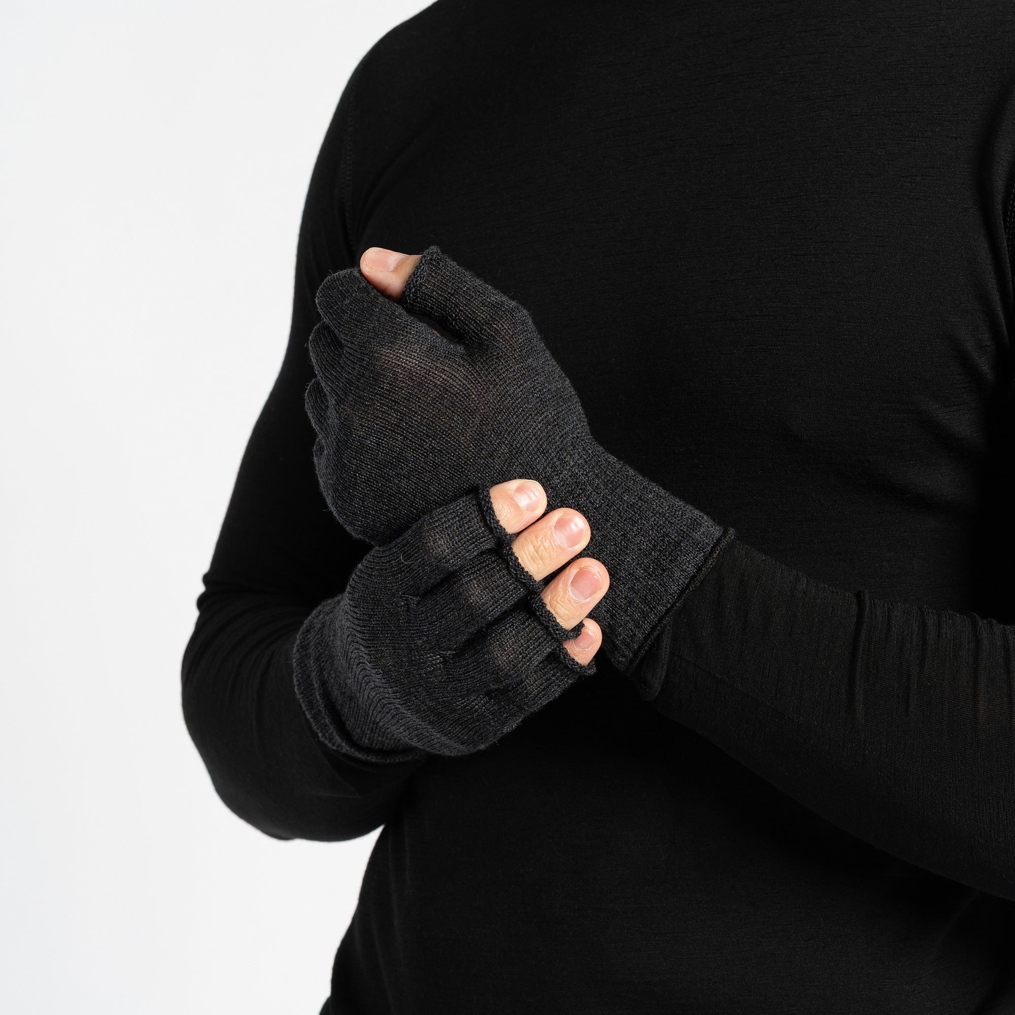 A person wearing a black long-sleeved shirt is shown from the chest up, putting on dark green fingerless gloves. The background is white.