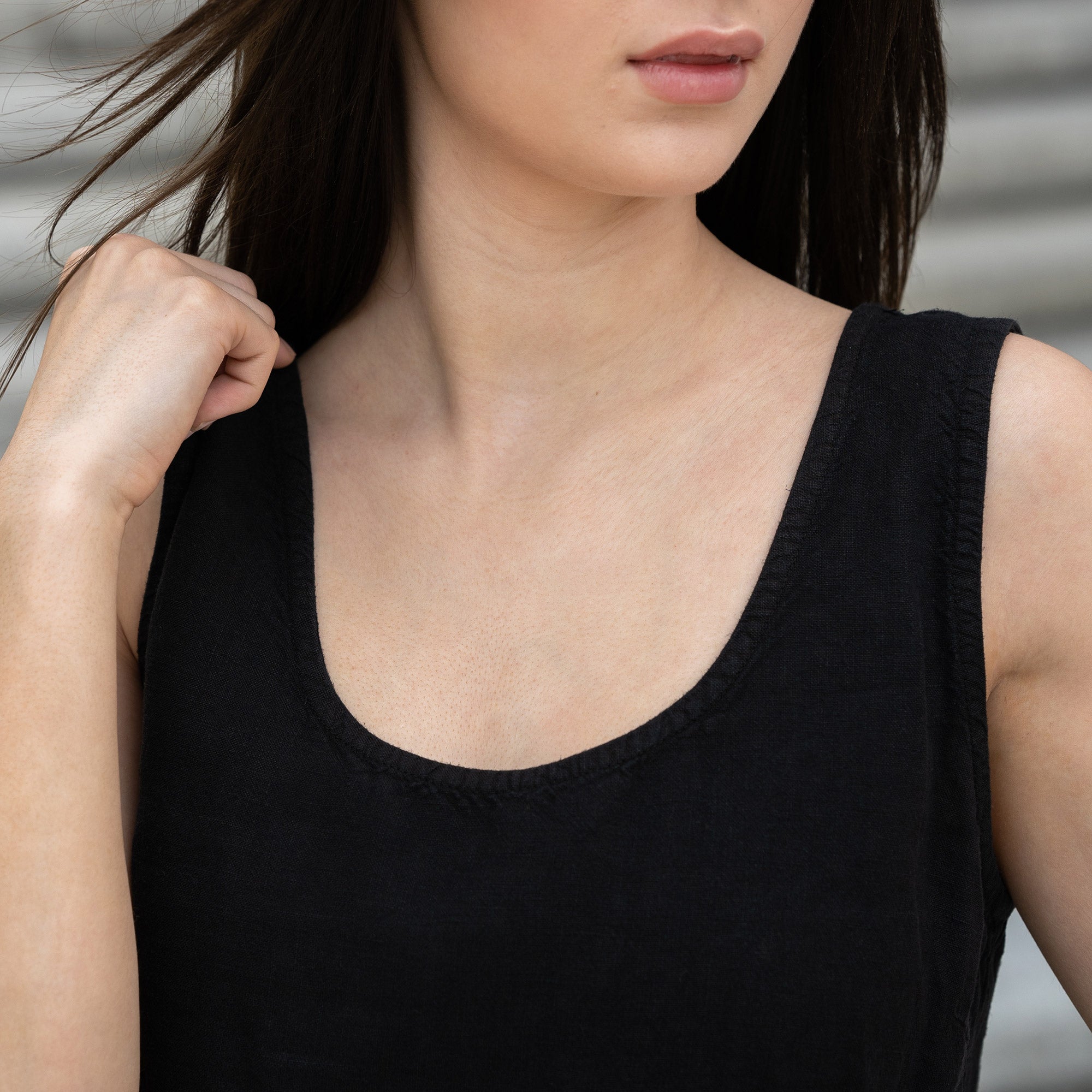 A young girl posing outdoors in a city on a concrete stairs, wearing linen pure black tank top Hana, and pure black pants dakota. 