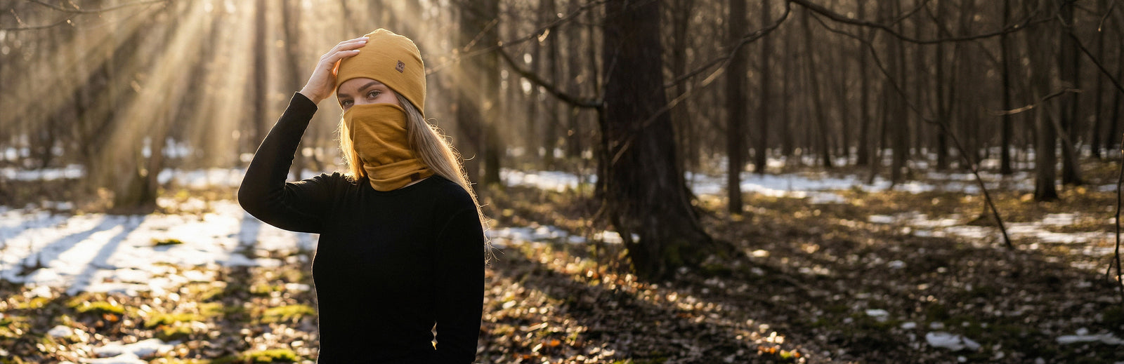 Woman wearing merino wool beanie and neck gaiter outdoors in a forest during cold weather.