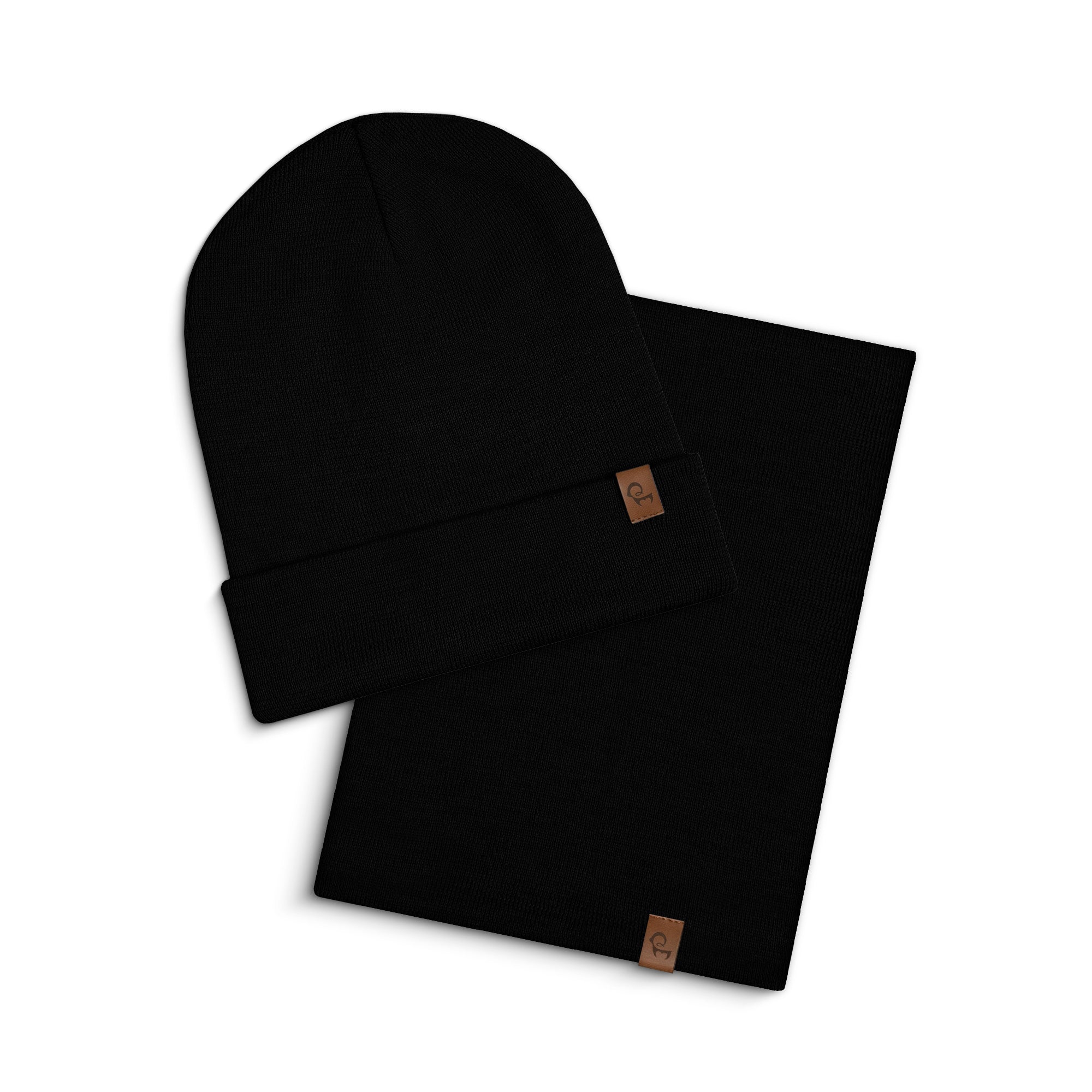 A studio shot on a white background showing a dark gray menique knitted beanie and a matching neck gaiter. The beanie is folded at the brim and placed on its side. The neck gaiter is laid flat next to it. Both items have a small, rectangular brown leather tag with rounded corners visible on them.