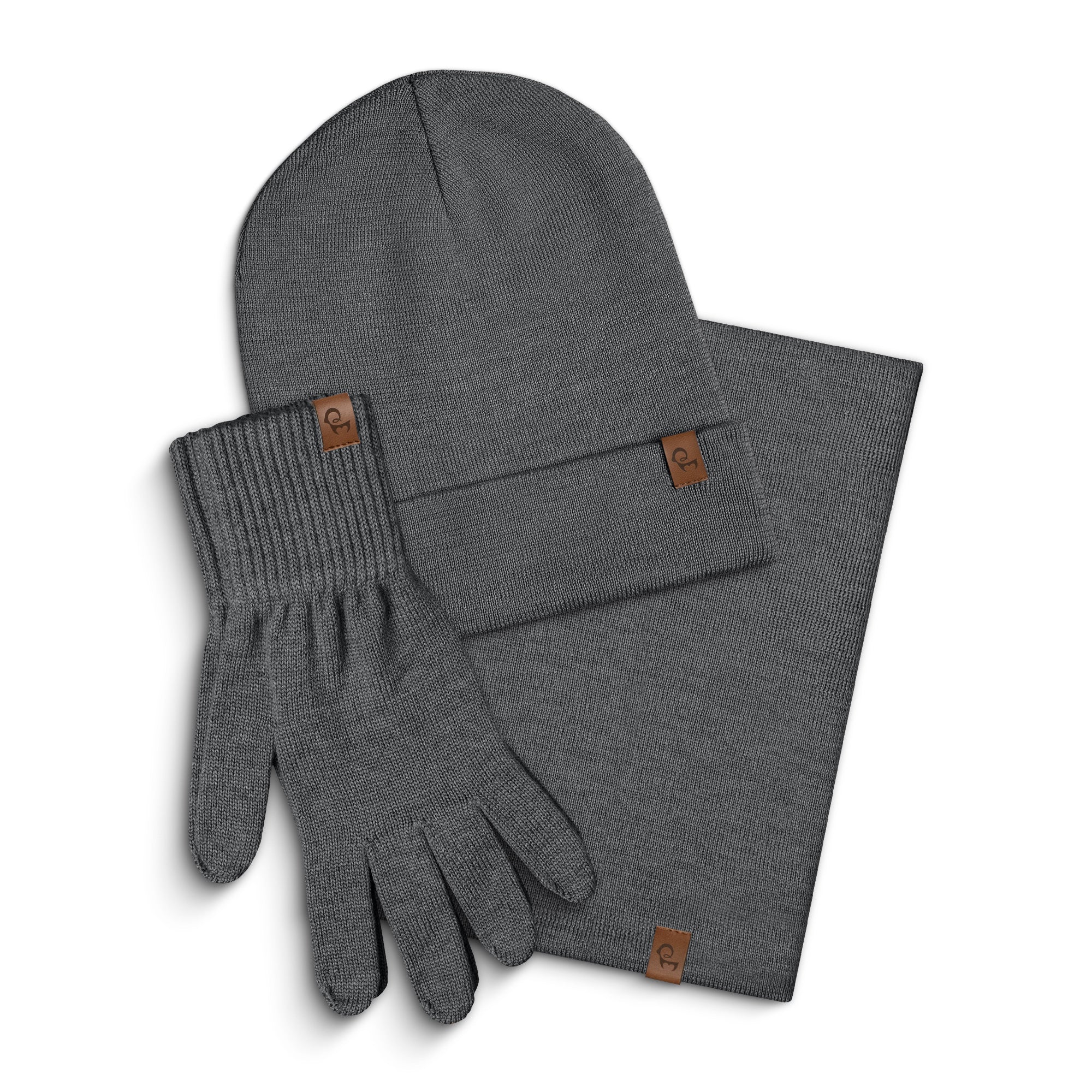 A set of creamy beige knitted accessories, including a beanie, a pair of gloves, and a gaiter, are arranged on a white background. Each item features a small, rectangular brown leather tag. The beanie is positioned at the top left, the gloves are below it, and the scarf is folded and placed to the right.