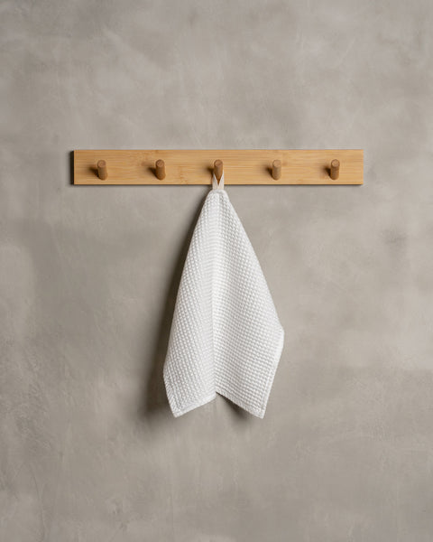 A gray wall with a wooden hanger. In the middle of it hangs a waffle face washcloth in pure white color.