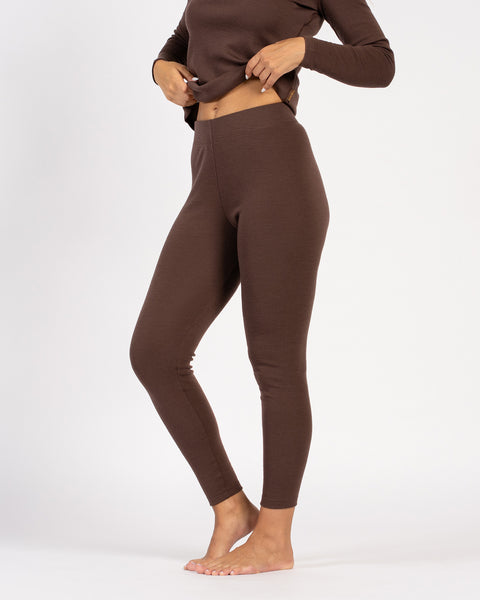Woman adjusting brown merino wool thermal top, showcasing leggings fit.