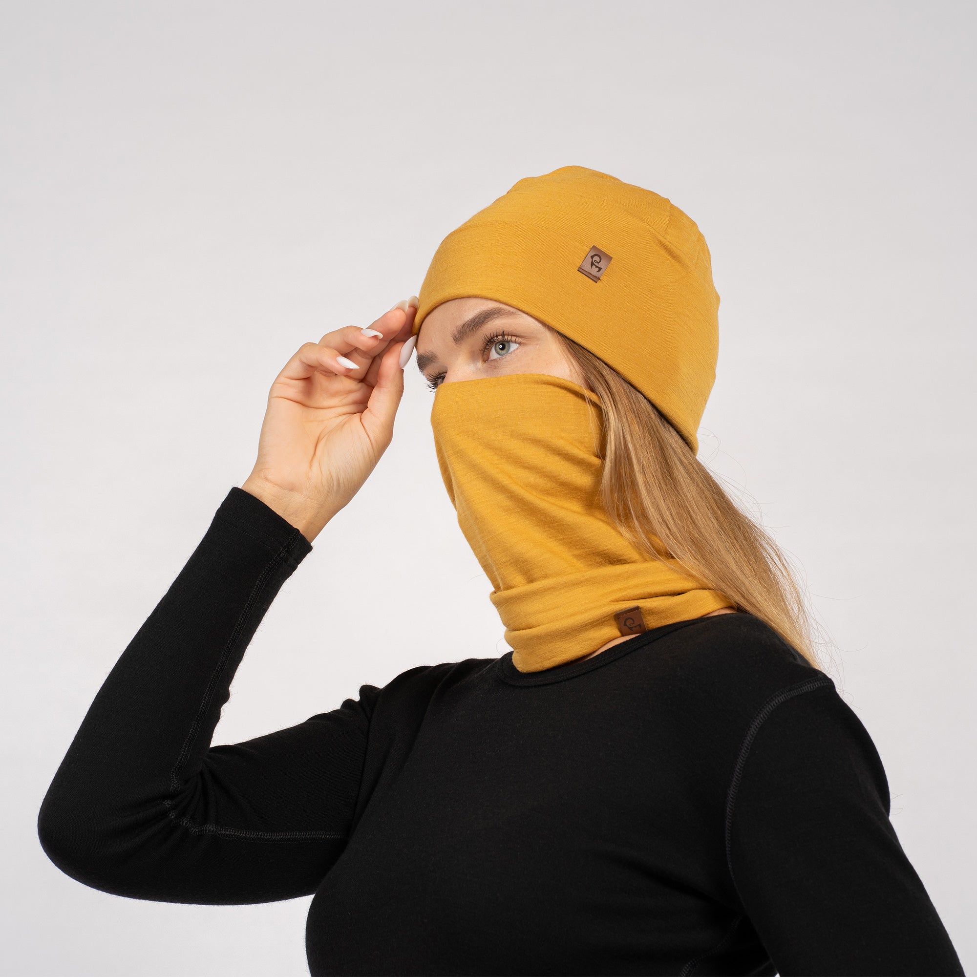 Woman in yellow Merino beanie and gaiter worn around neck, posing in black long sleeve top – side view.