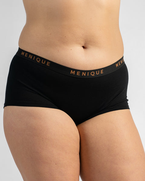 Front view of a model wearing black boy-short underwear with a black elastic waistband featuring text.