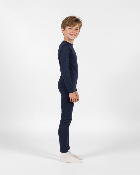 Young boy standing in side profile smiling at the camera, wearing a dark navy blue long-sleeve thermal base layer set and white socks against a plain white background.