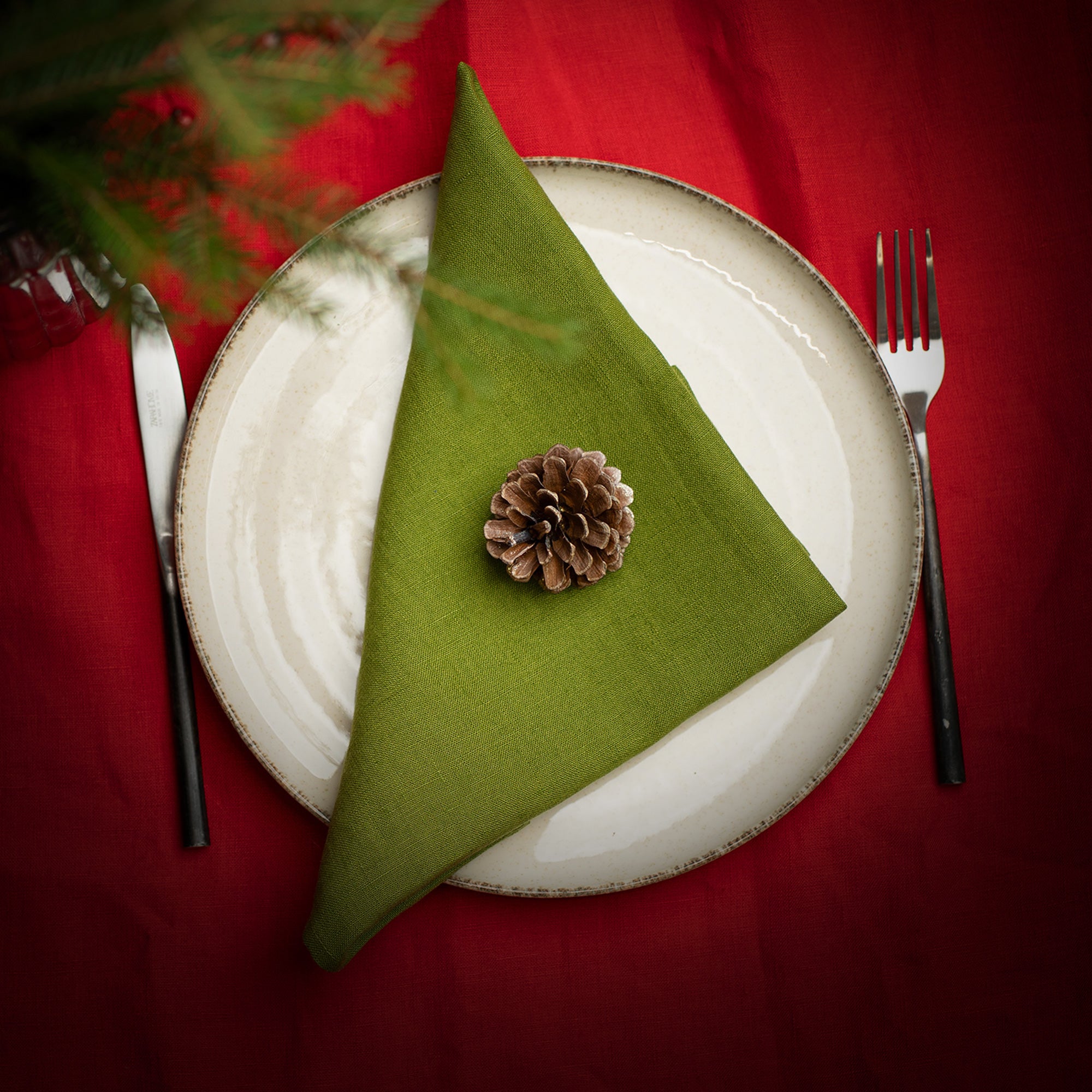 Green triangular napkin with a pine cone on a white plate with red tablecloth