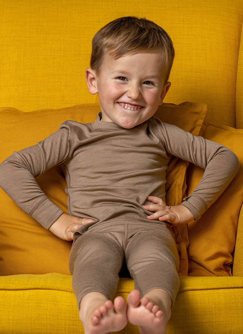 Smiling boy sitting on yellow armchair wearing beige loungewear set