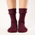 A person is shown from the mid-thigh down, wearing ribbed, royal cherry colos socks. The socks are pulled up to the mid-calf, and the person's feet are slightly apart against a plain white background. The lighting is even, highlighting the texture of the socks.