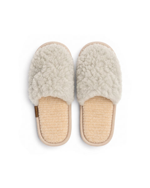 A top-down view of a pair of light gray fuzzy slip-on slippers with beige insoles and a "MENIQUE" tag on the side of the left slipper.