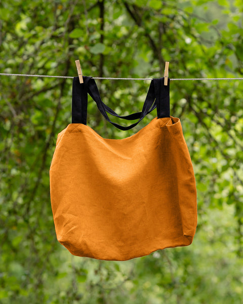 The menique linen tote bag in spicy yellow color with black handles hung on a clothesline outside.
