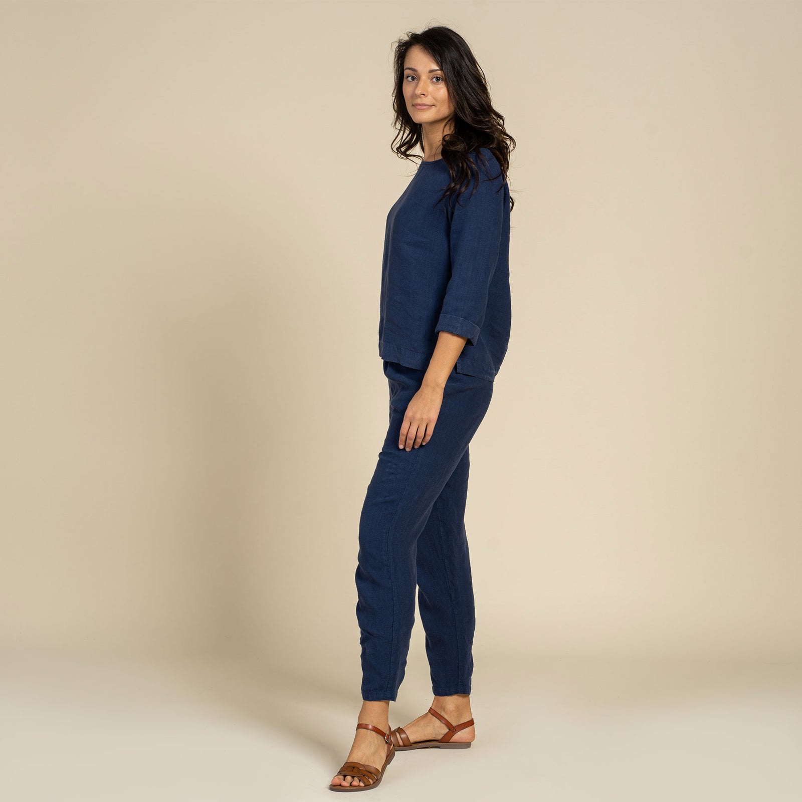 Person wearing storm blue linen menique pants and brown sandals on a neutral background