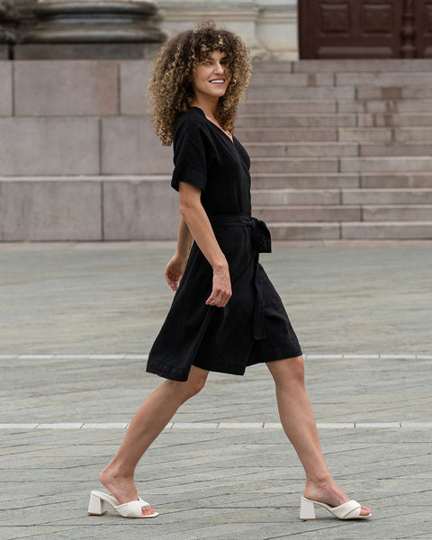 Woman outside in the city walking by and smiling with a pure black linen dress eliana.