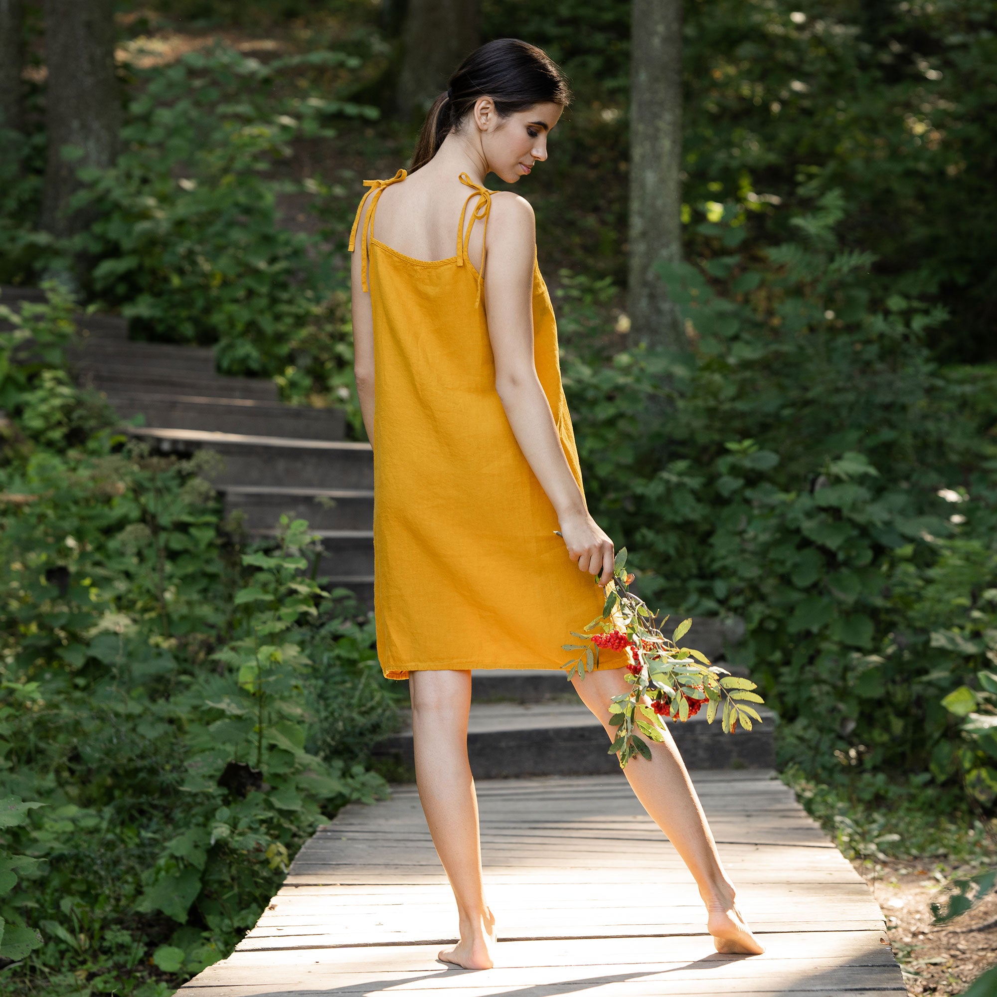 Woman wearing spicy yellow linen dress and standing in  the forest