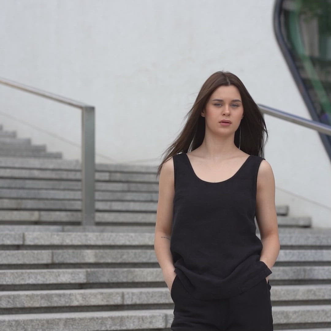 A young girl posing outdoors in a city on a concrete stairs, wearing linen pure black tank top Hana, and pure black pants dakota. 