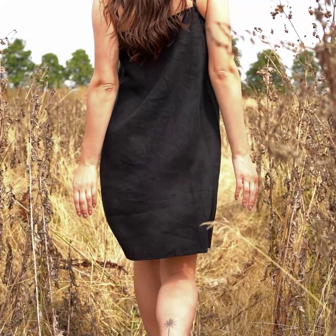 Woman walking through tall grasss and wearing linen dress in black color